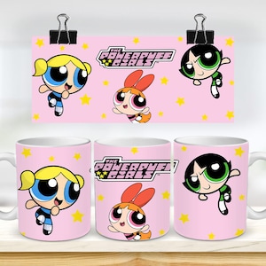 Puede incluir: Tres tazas de cerámica blanca con fondo rosa e imágenes de las Chicas Superpoderosas. Las tazas presentan a Bombón, Burbuja y Bellota, cada una con sus colores y peinados característicos. El texto "The Powerpuff Girls" está impreso en las tazas.