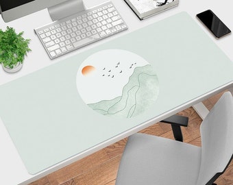 May include: A light green and white desk mat with a minimalist design featuring a stylized mountain range and a small orange sun. The design is surrounded by a circle and there are small black birds flying above the mountain range.