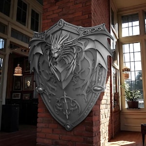 Puede incluir: Un gran escudo plateado con un diseño detallado de dragón. El escudo presenta la cabeza de un dragón con las fauces abiertas y alas. El escudo está montado en una pared de ladrillo rojo, mostrando un tema medieval o de fantasía.