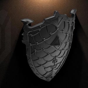 Puede incluir: Un escudo negro con un diseño intrincado, que presenta un patrón similar a una red y elementos decorativos. El escudo tiene una forma curva y está sobre un fondo oscuro con una superficie texturizada. El escudo tiene un logotipo en la parte inferior derecha.