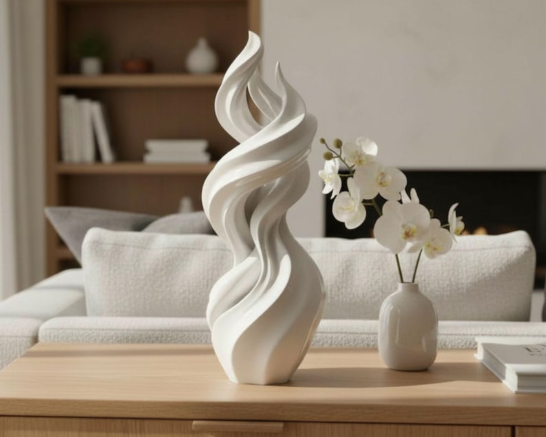 May include: A white, abstract sculpture with a swirling, flame-like design. The sculpture is placed on a wooden table, next to a small white vase with white orchids. The background includes a sofa, bookshelf, and fireplace.