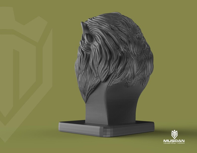 May include: A dark grey sculpture of a lion's head with detailed fur texture, mounted on a rectangular base. The background is a muted olive green. The logo "MUSDAN INDUSTRIAL TASARIM" is visible in the bottom right corner.
