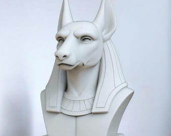 May include: A white bust of Anubis, the ancient Egyptian god of the afterlife, with a jackal head and human body. The sculpture features detailed facial features, tall ears, and a decorative collar. The bust is mounted on a rectangular base.