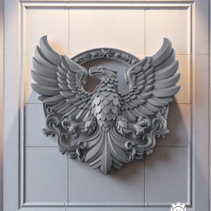Könnte beinhalten: Ein graues, dreidimensionales Adleremblem mit ausgebreiteten Flügeln, vor einer hellgrauen, getäfelten Wand. Der Adler ist von einem kreisförmigen Kranz und dekorativen Verzierungen umgeben. Das Emblem ist ein dekorativer Wandschmuck.