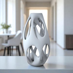 May include: A white, abstract ceramic vase with an open, lattice-like design. The vase has an elongated, oval shape with multiple openings and a smooth, matte finish. It is displayed on a white surface, suggesting a modern home decor item.