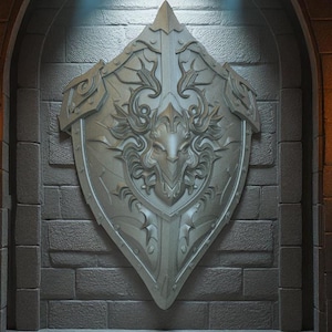 Pode incluir: Um escudo prateado e ornamentado com um design central de rosto de leão, montado em uma parede de tijolos texturizada. O escudo tem entalhes detalhados e um topo pontiagudo, sugerindo um tema medieval ou de fantasia. A iluminação destaca os detalhes.