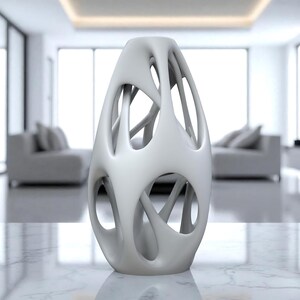 May include: A white, abstract vase with an open, cage-like design. The vase has an organic shape with multiple openings and a smooth, matte finish. It is displayed on a marble surface in a modern interior setting.