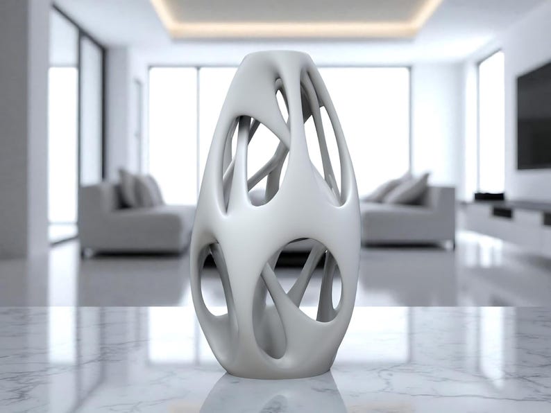 May include: A white, abstract vase with an open, cage-like design. The vase has an organic shape with multiple openings and a smooth, matte finish. It is displayed on a marble surface in a modern interior setting.