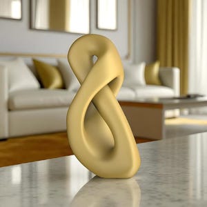 May include: A gold-colored, abstract sculpture in the shape of an infinity symbol. The sculpture is smooth and stands on a marble surface. The background includes a white sofa with gold pillows and a coffee table, suggesting a modern home decor theme.