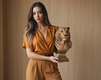 May include: A tan and brown tiger head bust sculpture mounted on a pedestal base. The tiger features detailed facial carvings with dark stripes and a smooth finish, crafted as a decorative object for display on a flat surface or shelf.