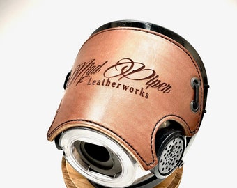 May include: A brown leather motorcycle helmet with a black base and a silver vent. The helmet has the text "Mad Piper Leatherworks" embossed on the front.