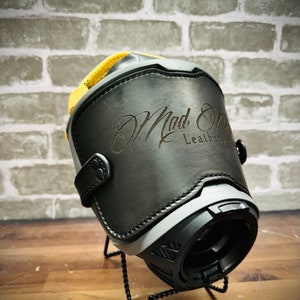May include: Black leather motorcycle boot with a gray and black sole. The boot has a yellow strap and a Mad Ox Leather logo embossed on the side.