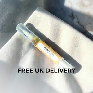 May include: A pen-style cuticle oil applicator with a yellow label reading "SUMMER HEAT". The applicator is clear with a white applicator tip and a clear cap. It rests on a white surface with a marble effect background.