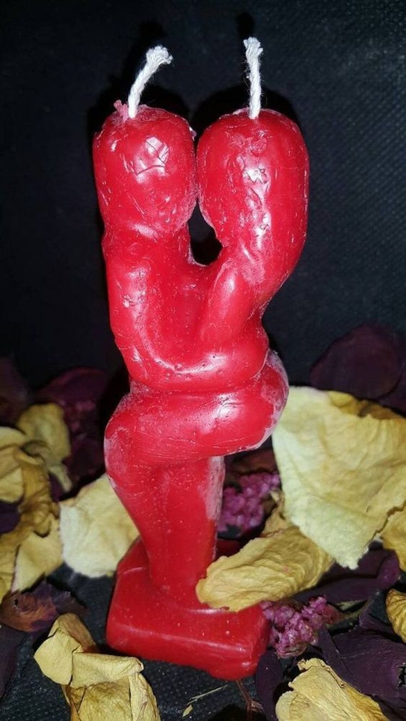 Pode incluir: Uma vela vermelha em forma de duas figuras abra&ccedil;ando-se. A vela est&aacute; sobre uma base e tem uma superf&iacute;cie texturizada.