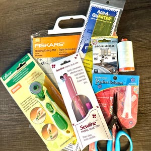 May include: A collection of sewing tools including a rotary cutter, cutting mat, fabric glue pen, scissors, thread, and needles. The items are packaged in various colors, including green, orange, pink, and blue.