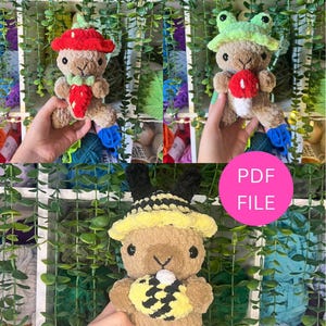 Op de afbeelding: Drie handgemaakte gehaakte pluche speelgoed. Eén is een bruin konijn met een rode aardbeienhoed en een aardbei. Een andere is een bruin konijn met een groene kikkerhoed en een rode paddenstoel. De laatste is een bruin konijn met een bijenhoed en een gele honingraat.