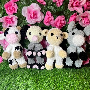 May include: Four crocheted stuffed animals: a cow, a pig, a lamb, and a donkey. The animals are all white with black spots or stripes, and they have pink noses and eyes. They are sitting on a green grassy surface.