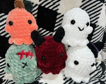 May include: Five crocheted Halloween-themed plush toys. A green zombie, an orange pumpkin, a white ghost, a red devil, and a white ghost with a purple hat.