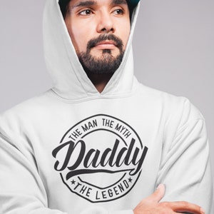 May include: A white hooded sweatshirt with a black circle graphic that says "The Man The Myth Daddy The Legend".