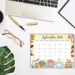 May include: A desk calendar for September 2026 with a watercolor design. The calendar features a cream-colored background with autumn leaves and decorative elements. A cup of coffee, a pen, and glasses are on the desk.