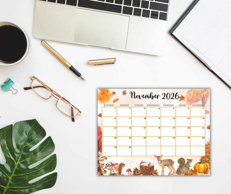 Puede incluir: Un calendario de escritorio para noviembre de 2026 con tem&aacute;tica oto&ntilde;al. El calendario presenta un dise&ntilde;o de cuadr&iacute;cula con un borde decorativo de follaje oto&ntilde;al, calabazas, ardillas y un ciervo. Est&aacute; rodeado por un port&aacute;til, un bol&iacute;grafo, gafas y una taza de caf&eacute;.