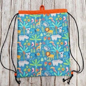 May include: A blue drawstring bag with a colourful jungle animal print. The bag features a variety of animals including hippos, giraffes, monkeys, toucans, and koalas. The bag has orange drawstrings and black cords.