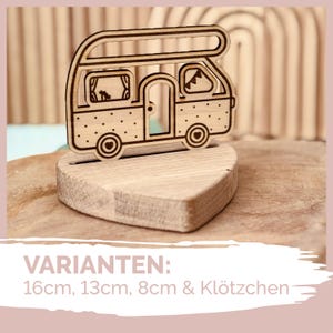 May include: Wooden cutout of a camper van with a heart-shaped base. The camper van is brown with a white roof and windows. The text "VARIANTEN: 16cm, 13cm, 8cm & Klötzchen" is visible below the camper van.