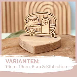 May include: Wooden cutout of a camper van with a heart-shaped base. The camper van has a small window and a flag on top. The text "VARIANTEN: 16cm, 13cm, 8cm & Klötzchen" is visible below the cutout.