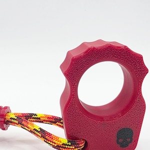 May include: A red, textured ring with a black skull emblem and a multi-colored rope. The ring has a unique, ridged design around the outer edge. The rope is a mix of yellow, orange, and black.