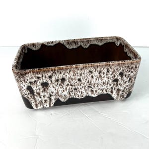 May include: Rectangular ceramic planter with a dark brown interior and exterior. The exterior features a textured, dripped glaze in shades of brown and white, creating a unique, decorative effect. The planter has a rectangular shape.