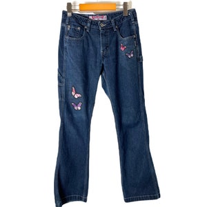 May include: Dark blue denim jeans with butterfly embroidery. The butterflies are pink, purple, and white.