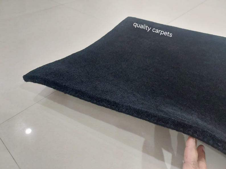 May include: A thick, solid black rectangular carpet with a dense, textured pile surface. The text "quality carpets" is printed in white on the upper portion of the carpet. The material appears firm and uniform in color throughout the entire piece.