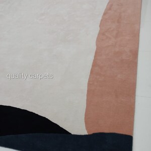 May include: Abstract area rug with a white, pink, black, and blue design. The rug has a modern, contemporary style. The text "quality carpets" is visible in the lower left corner of the rug.