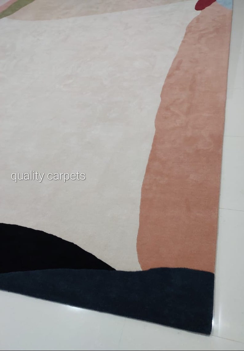 May include: Abstract area rug with a white, pink, black, and blue design. The rug has a modern, contemporary style. The text "quality carpets" is visible in the lower left corner of the rug.