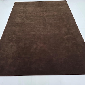 May include: A rectangular area rug in a solid dark brown color. The rug features a short, dense pile texture that creates subtle variations in shade across the surface depending on the light, providing a uniform and consistent appearance.