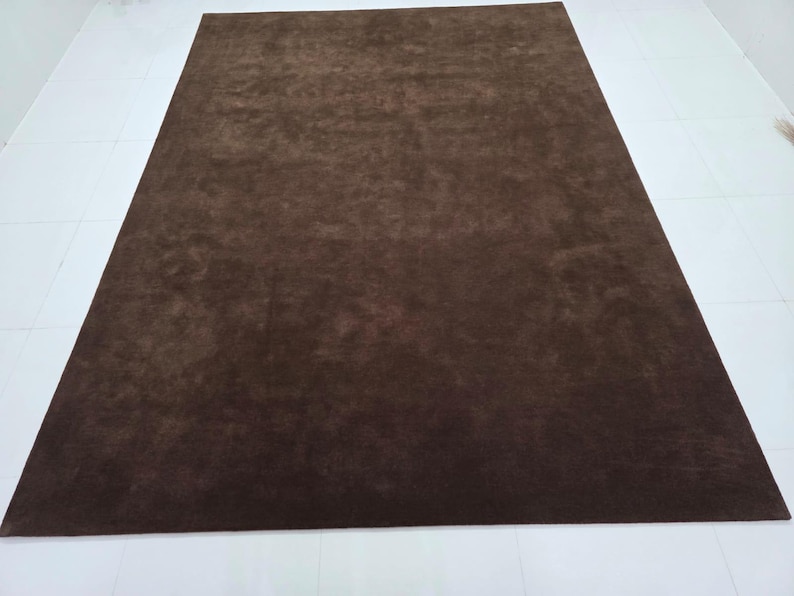 May include: A rectangular area rug in a solid dark brown color. The rug features a short, dense pile texture that creates subtle variations in shade across the surface depending on the light, providing a uniform and consistent appearance.