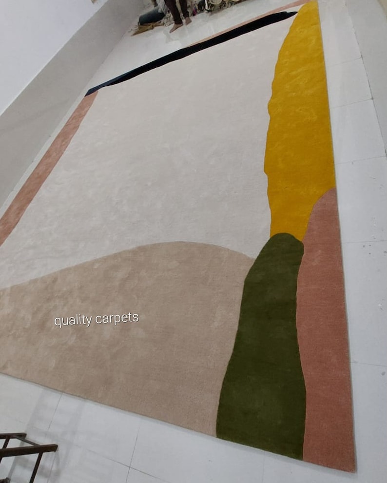 May include: Abstract area rug with a beige background, featuring large shapes in shades of pink, green, and yellow. The text "quality carpets" is visible in the lower left corner.
