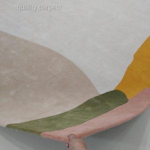 May include: A close-up of a multi-coloured rug with a geometric design. The rug is made of soft, plush material and features shades of pink, green, yellow, and white. The text "quality carpets" is visible in the top left corner of the image.