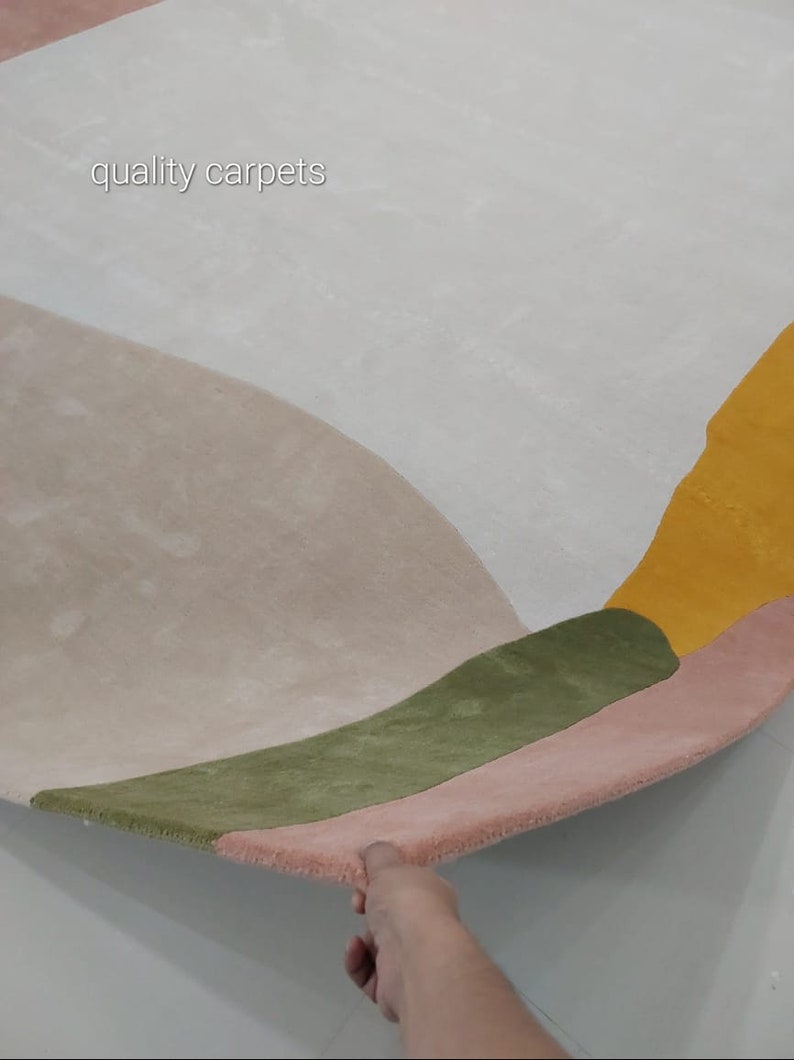 May include: A close-up of a multi-coloured rug with a geometric design. The rug is made of soft, plush material and features shades of pink, green, yellow, and white. The text "quality carpets" is visible in the top left corner of the image.