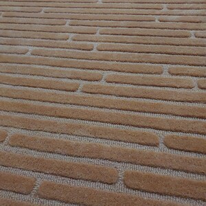 Puede incluir: Primer plano de una alfombra marrón con un patrón texturizado de líneas horizontales y formas redondeadas.