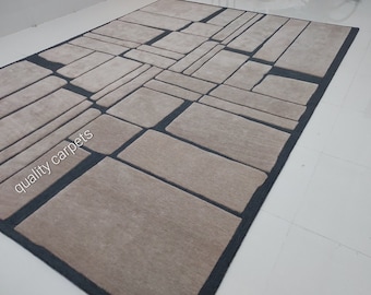 Puede incluir: Una alfombra beige y gris con un patrón geométrico. La alfombra está hecha de un material suave y mullido y tiene un diseño moderno. El texto "quality carpets" es visible en la esquina inferior izquierda de la alfombra.