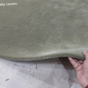 May include: A sage green carpet with a thick, plush pile texture. The surface is uniform in color and features a soft, dense appearance. The text "quality carpets" is printed in white in the upper left corner of the image.