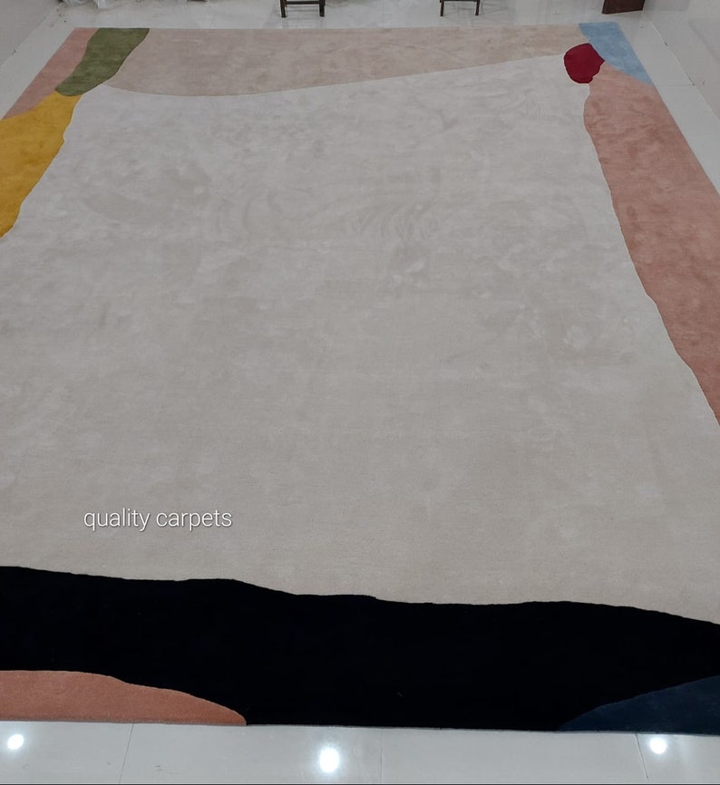 May include: A modern abstract area rug with a white background and geometric shapes in shades of pink, yellow, green, blue, and black. The rug has the text "quality carpets" in the centre.