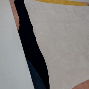 May include: Abstract area rug with black, yellow, pink, and white geometric shapes. The rug has a soft, plush texture. "quality carpets" is printed in the lower right corner.
