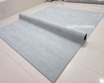 May include: A large, pale blue rug with a rolled edge. The rectangular rug is made of a soft material. The text "Qualitycarpets" is visible on the rug's surface.