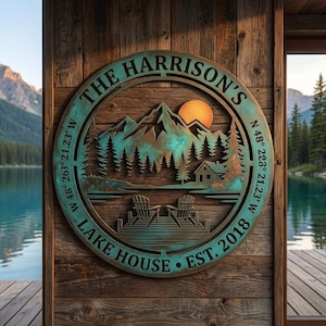 May include: A circular metal wall sign with a teal and copper patina finish featuring a mountain landscape, a cabin, and two chairs on a dock. The text reads THE HARRISON'S, LAKE HOUSE, EST. 2018, and coordinates W 48° 263' 21.23" W N 48° 223' 21.23" W.
