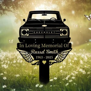 May include: Black metal memorial stake featuring a classic Chevrolet truck design. The stake includes the text "In Loving Memorial Of Russel Smith 1963-2025" with angel wings and a heart. Butterflies and flowers are in the background.