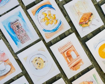 May include: A collection of watercolor paintings on white paper, depicting various scenes including architecture, food, and landscapes. The paintings feature a range of colors and styles, showcasing a travel or culinary theme.