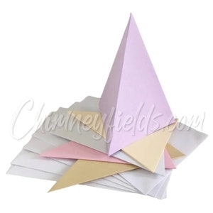 Puede incluir: Una pila de cuadrados de papel doblados en blanco, rosa y beige con una pirámide lavanda en la parte superior.