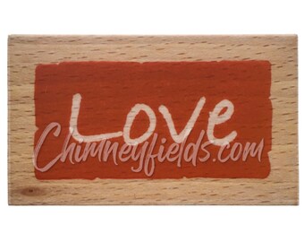 May include: A wooden sign with a red background and the word "LOVE" written in white paint. The sign also includes the website "Chimneyfields.com" in white paint.
